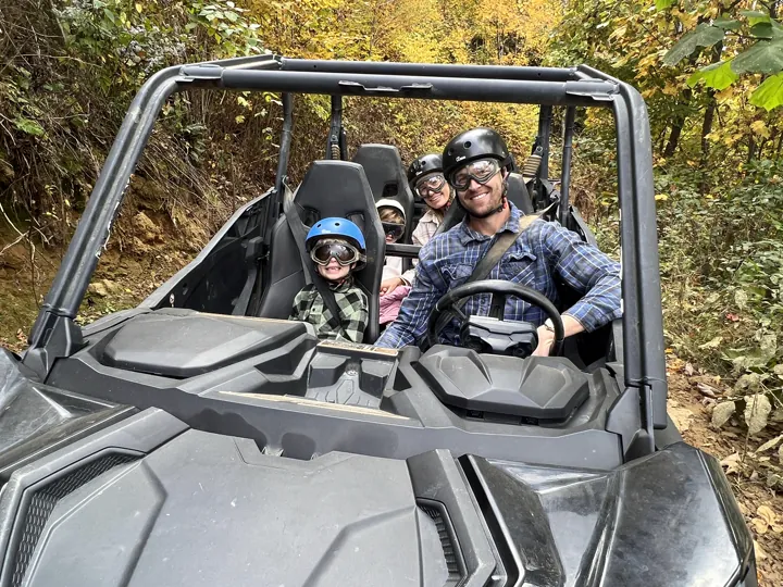 A family riding in a UTV, a father at the wheel with a child in a blue helmet beside him