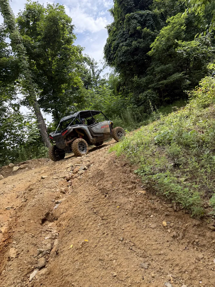 A UTV climbing a steep dirt hillside on a forested trail
