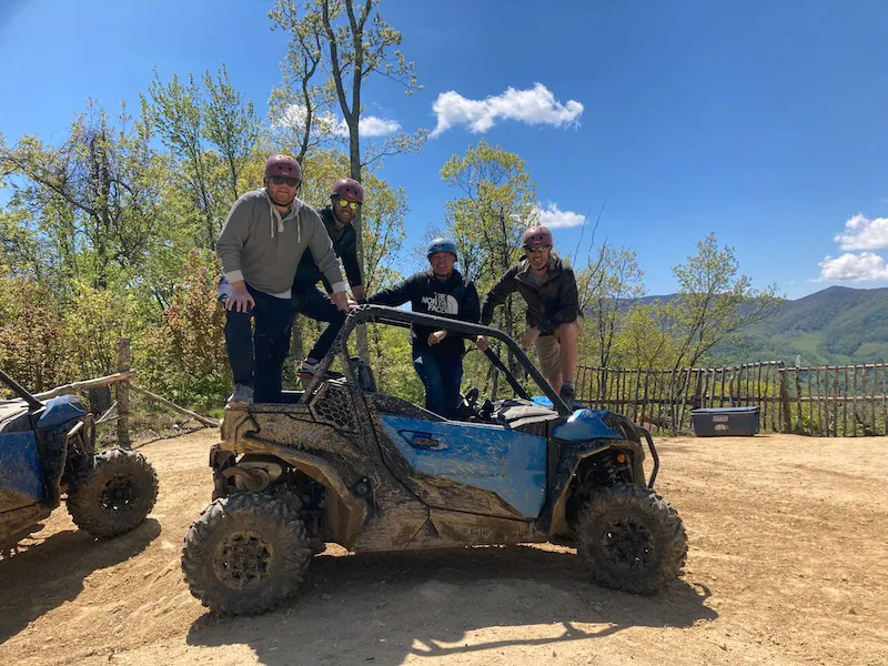 Riders standing on a mud-covered UTV at the summit overlook