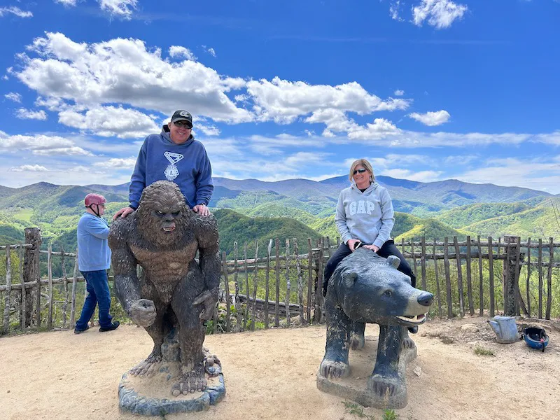Two visitors beside the carved bear sculptures at the overlook, Appalachian ridgeline behind