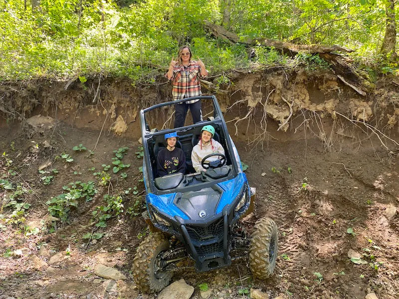 A blue UTV climbing a dirt bank while two riders watch from above