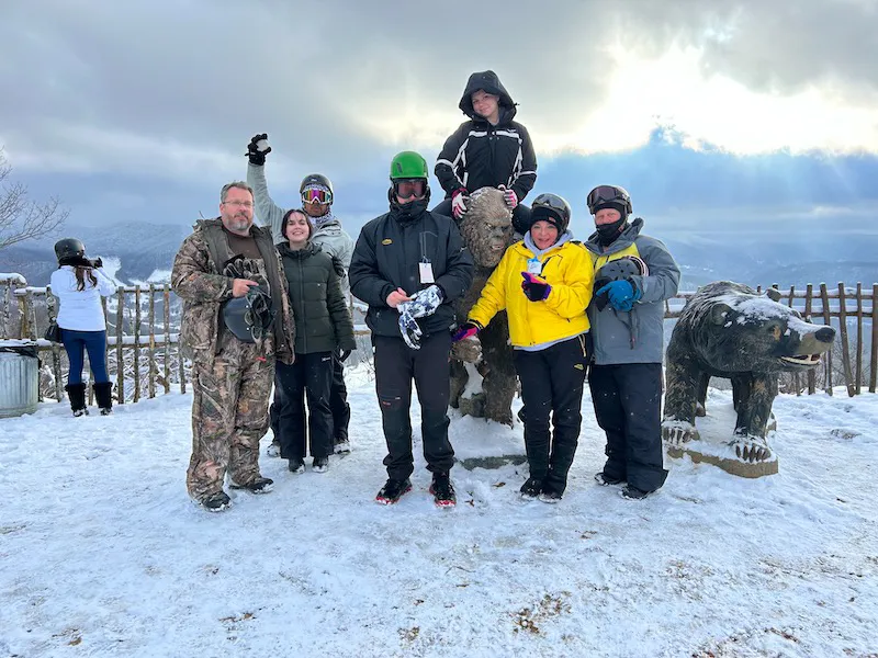 A bundled-up group posing in the snow beside the bear sculpture at the overlook