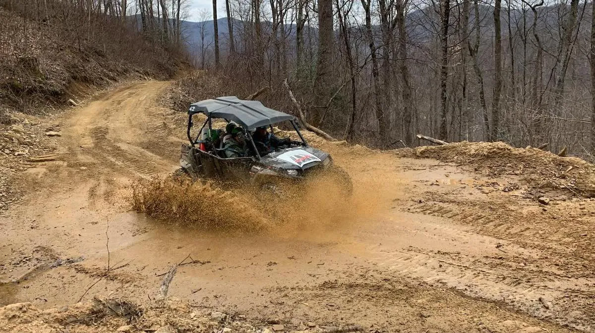 A UTV kicking up a cloud of dust through a turn on the mountain trail