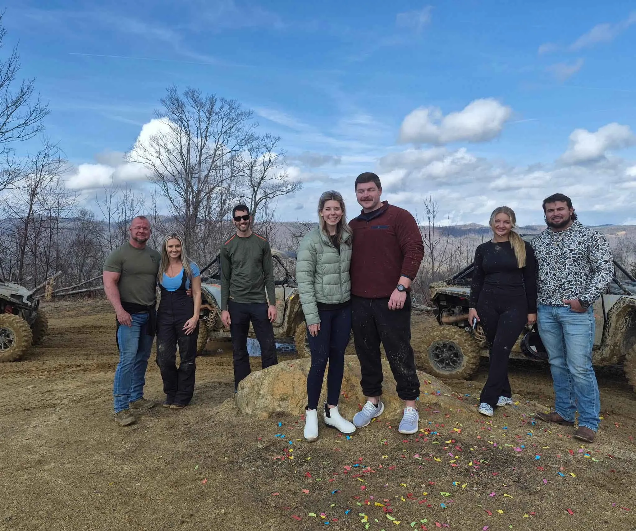 A group of seven posing at the summit overlook with the UTVs behind them