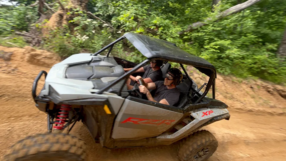 A gray Polaris RZR XP carving through a dirt trail with two riders aboard